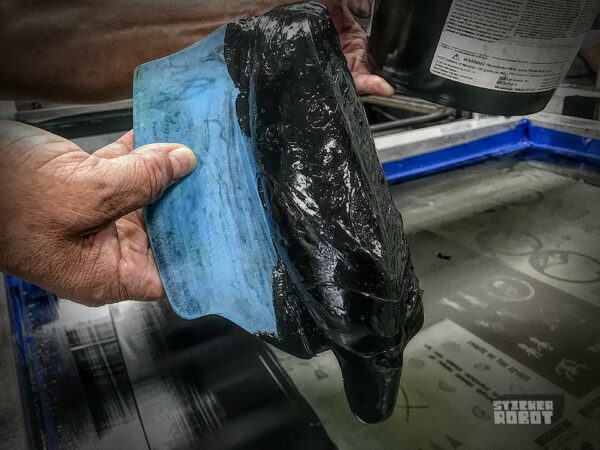 Silkscreen printing ink being applied through a mesh screen with a hand squeegee